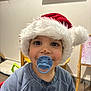 Lyssandro a rejoint le concours — aidez-le/la à gagner de superbes lots ! baby, blue_pacifier, chair, child, cute, easel, floor, happy, headwear, holiday, home, indoor, messy_face, pacifier, person, santa_hat, smiling, sweatshirt, toddler, wooden_furniture