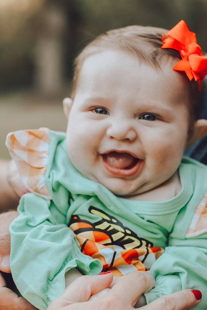 Oaklynne joined the competition — help win amazing prizes! baby, baby_toddler_clothing, cheek, chin, dress, eye, facial_expression, grass, happy, head, iris, lip, mouth, nose, orange, person, pink, plant, skin, smile