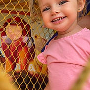 Léonie participe au concours pour gagner de l'argent avec cette photo : toddler, child, smile, pigtails, pink_shirt, netting, playground, face, happy, portrait, colorful_background, mural, young_child, outdoor, cute, person, fun, candid, daylight, joy