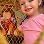 toddler, child, smile, pigtails, pink_shirt, netting, playground, face, happy, portrait, colorful_background, mural, young_child, outdoor, cute, person, fun, candid, daylight, joy