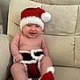 baby, infant, smiling, santa_hat, christmas_outfit, red_booties, crochet_clothing, cute, holiday, festive, indoor, armchair, beige_furniture, child, happy, portrait, holiday_season, cozy, cute_baby, seasonal