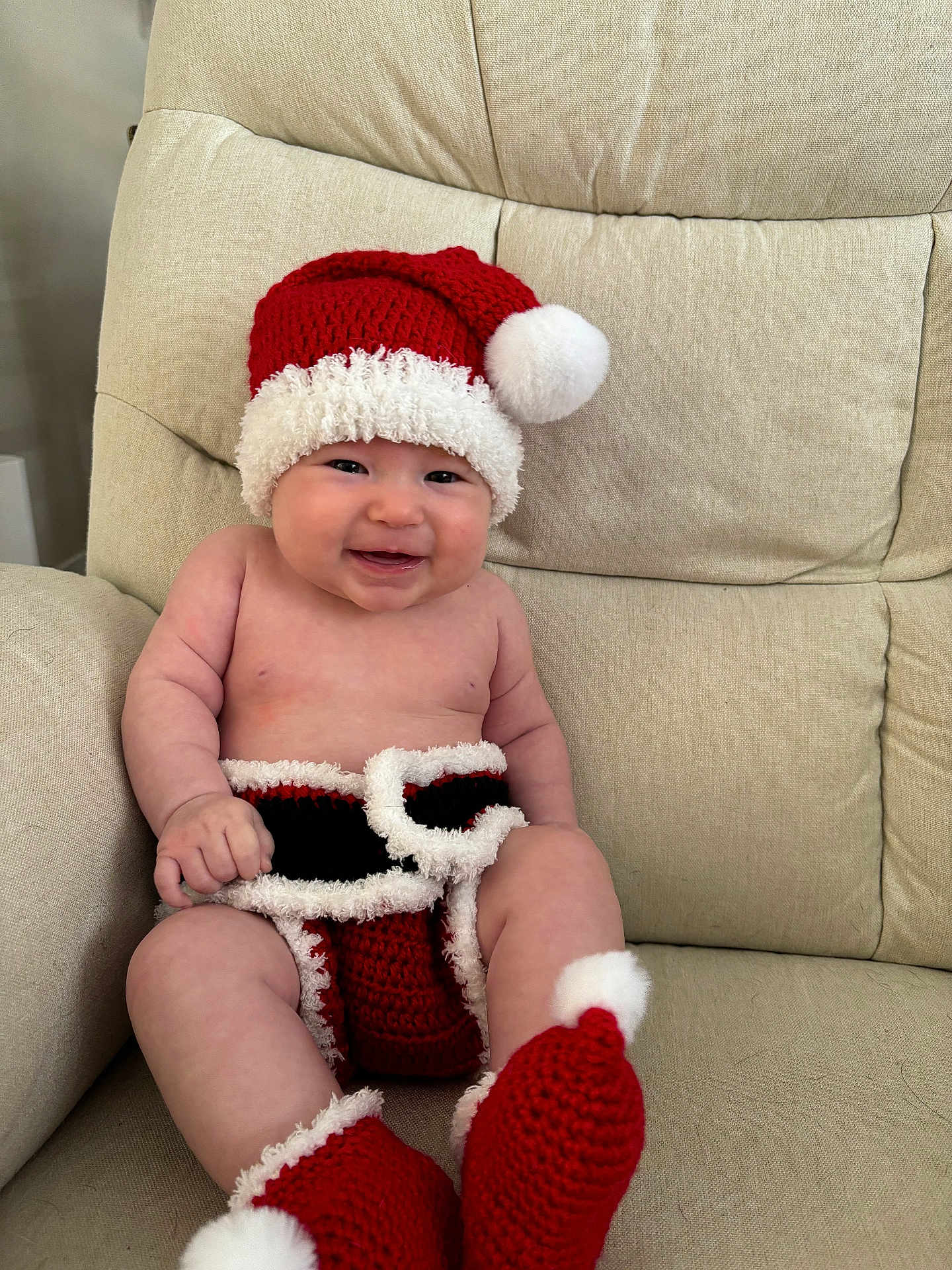 Millie joined the competition — help win amazing prizes! baby, infant, smiling, santa_hat, christmas_outfit, red_booties, crochet_clothing, cute, holiday, festive, indoor, armchair, beige_furniture, child, happy, portrait, holiday_season, cozy, cute_baby, seasonal