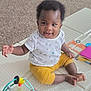 baby, child, smiling, sitting, indoors, toy, play_mat, white_shirt, yellow_pants, happy, infant, cute, carpet, playtime, colorful_toy, person, portrait, young_child, hand, feet