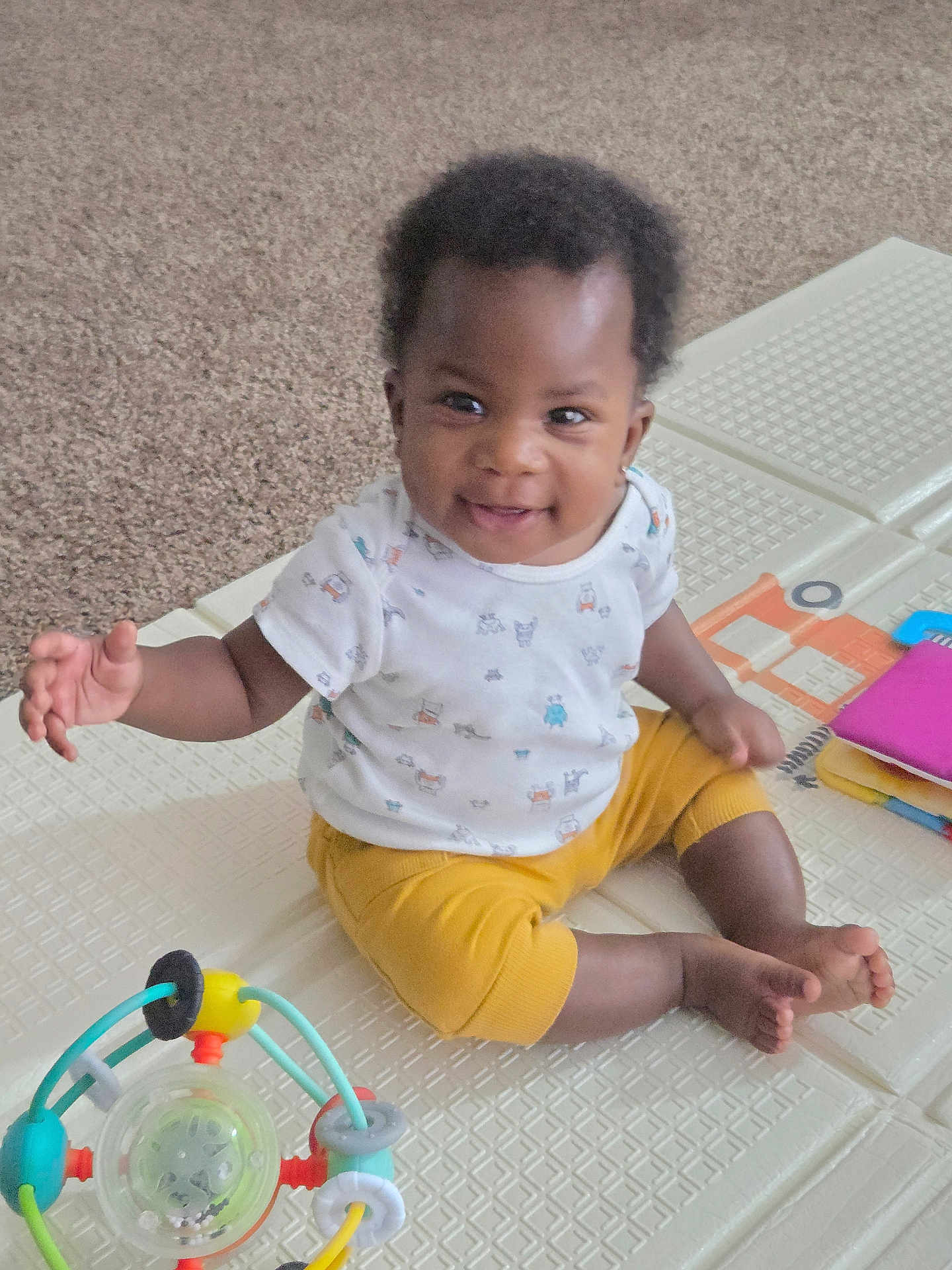 Adesewa joined the competition — help win amazing prizes! baby, child, smiling, sitting, indoors, toy, play_mat, white_shirt, yellow_pants, happy, infant, cute, carpet, playtime, colorful_toy, person, portrait, young_child, hand, feet