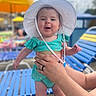 baby, child, smiling, white_hat, turquoise_outfit, hands, adult, poolside, lounge_chair, yellow_umbrella, summer, outdoor, sunny, happy, person, infant, cute, vacation, bright, daytime