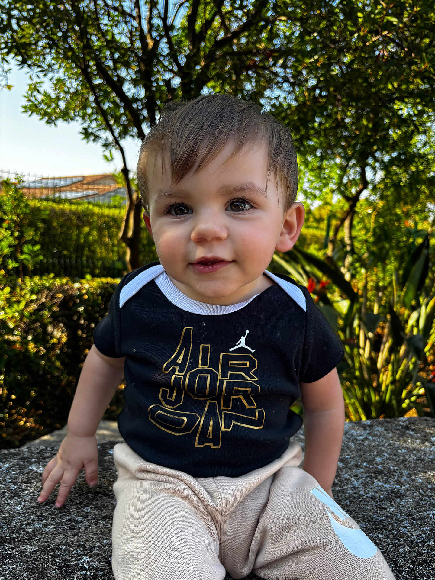 Leyandro participe au concours pour gagner de l'argent avec cette photo : child, toddler, baby, portrait, outdoor, greenery, smile, eyes, face, hair, shirt, pants, sitting, stone_ledge, sunlight, tree, leaves, daylight, cute, park