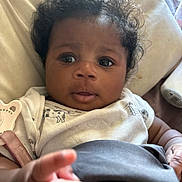 Zuri joined the competition — help win amazing prizes! baby, infant, child, curly_hair, face, eyes, hand, clothing, blanket, closeup, portrait, indoor, cute, skin, expression, person, young, cozy, reaching, soft