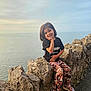 black_tshirt, camouflage_pants, casual_clothing, child, cloudy_sky, coast, daylight, happy, nature, ocean, outdoor, portrait, posing, rocks, sandals, scenery, sea, smiling, sunset, young