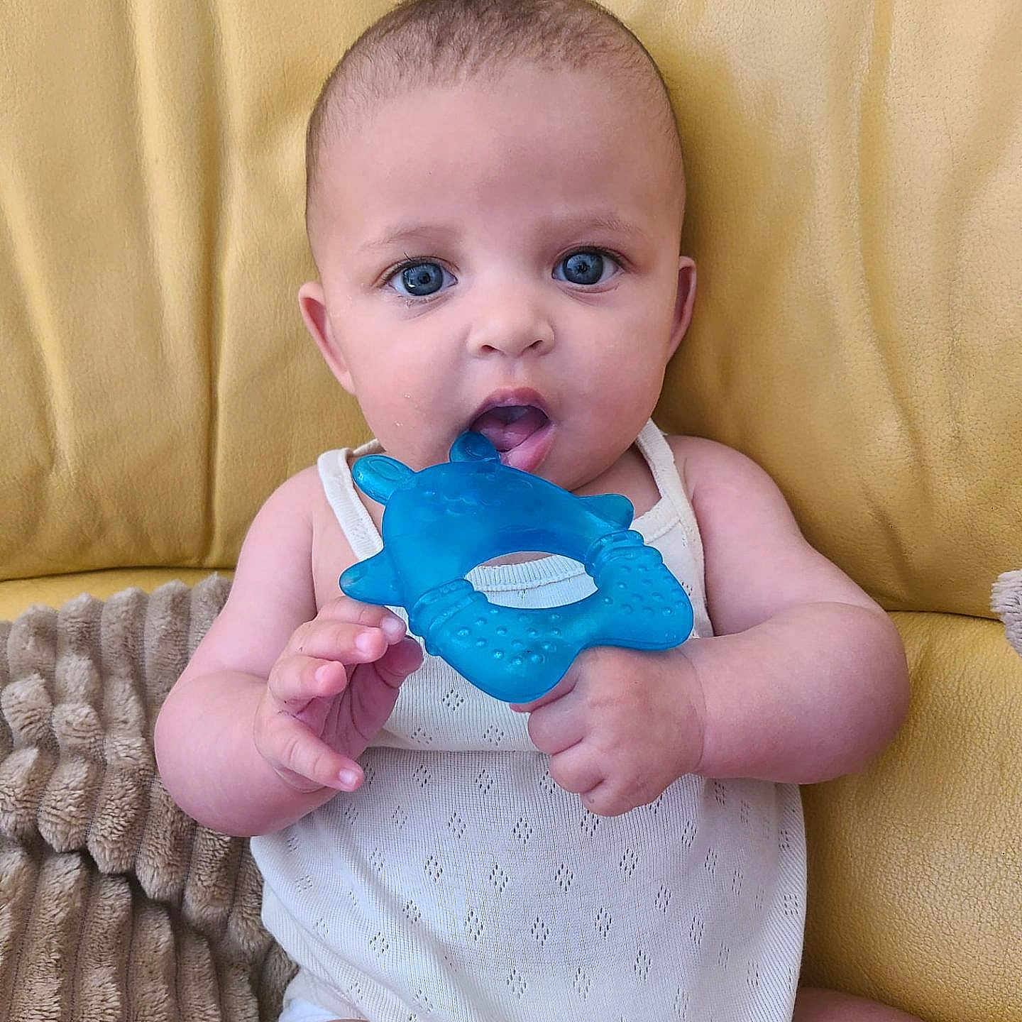 Andréa participe au concours pour gagner de l'argent avec cette photo : baby, blanket, blue_eyes, child, comfort, cute, expression, face, hand, indoors, infant, mouth, portrait, sitting, skin, teether, toy, white_outfit, yellow_couch, young