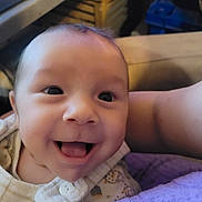 Thomas participe au concours pour gagner de l'argent avec cette photo : apparel, baby, babywear, blanket, closeup, clothing, cozy, cute, expression, eyes, face, happy, head, indoors, infant, person, portrait, skin, smiling, tongue_out