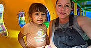 Blanca joined the competition — help win amazing prizes! child, toddler, mother, adult, smiling, portrait, selfie, indoor, playground, play_structure, yellow_slide, colorful, family, parent, daughter, sitting, casual_clothing, overalls, pink_shorts, backpack