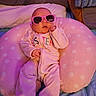 baby, infant, pink_sunglasses, polka_dot, cushion, blanket, sleepwear, bedroom, soft_lighting, cute, child, relaxed, indoors, person, portrait, sleeping, cozy, comfort, fashion, accessory