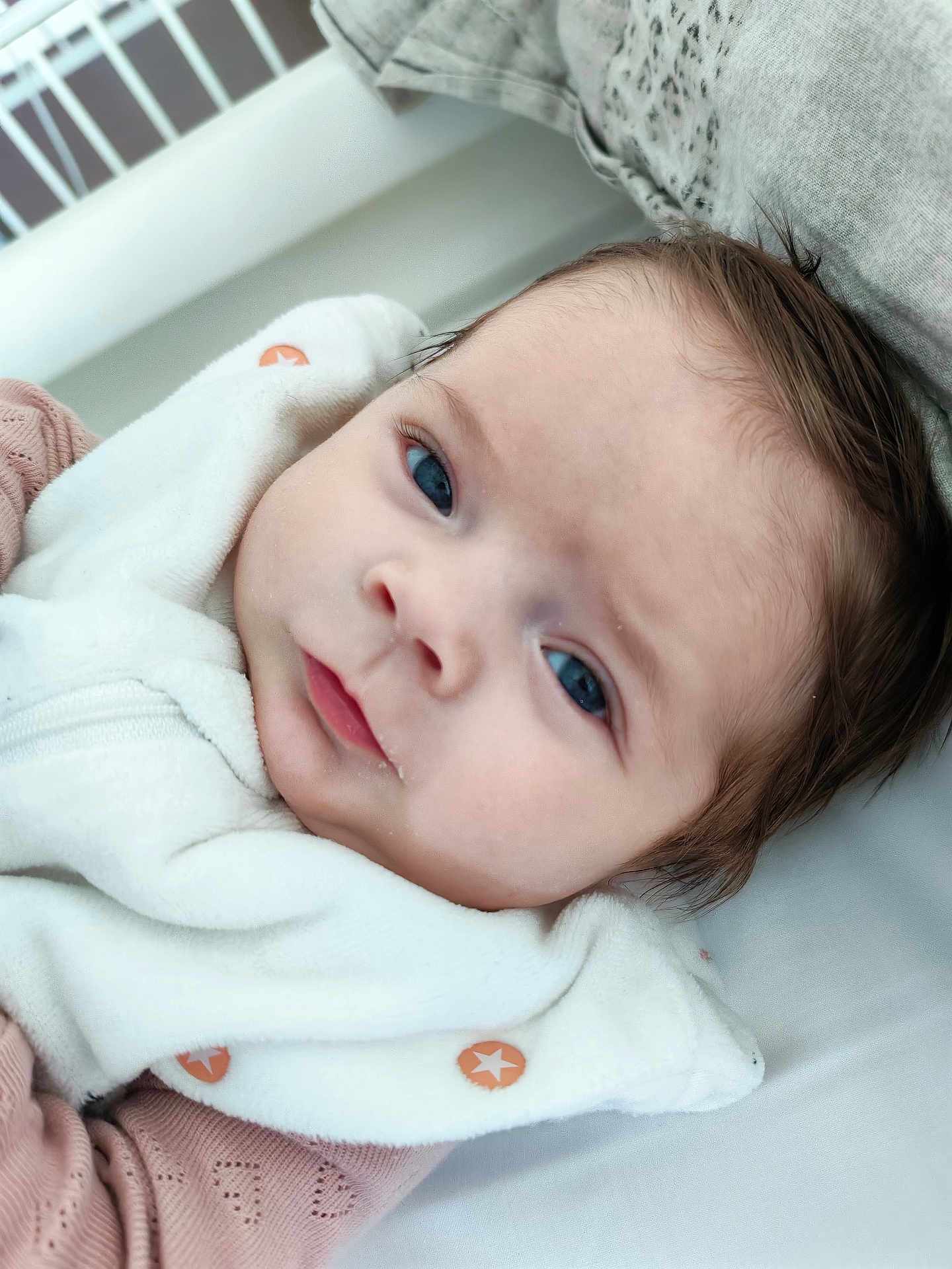 Alessia a rejoint le concours — aidez-le/la à gagner de superbes lots ! baby, infant, newborn, face, blue_eyes, hair, lips, blanket, bedding, crib, portrait, close_up, skin, gaze, eyelashes, swaddle, onesie, star_button, cute, adorable