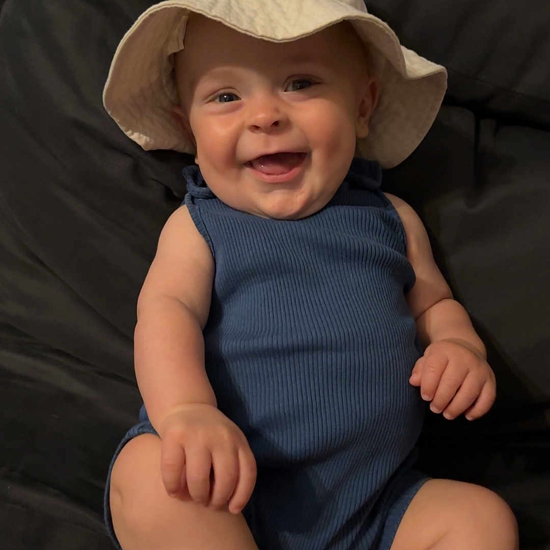 Eden a rejoint le concours — aidez-le/la à gagner de superbes lots ! baby, blue_clothing, casual, child, couch, cute, dark_background, face, happy, hat, headwear, indoors, infant, one_person, plush, portrait, relaxed, sitting, skin, smiling