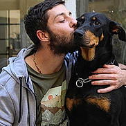 Biancka participe au concours pour gagner de l'argent avec cette photo : man, dog, pet, affection, kiss, beard, black_and_tan, collar, indoor, casual_clothing, hoodie, portrait, friendship, animal, canine, companion, love, human, closeup, expression