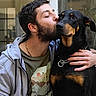 man, dog, pet, affection, kiss, beard, black_and_tan, collar, indoor, casual_clothing, hoodie, portrait, friendship, animal, canine, companion, love, human, closeup, expression