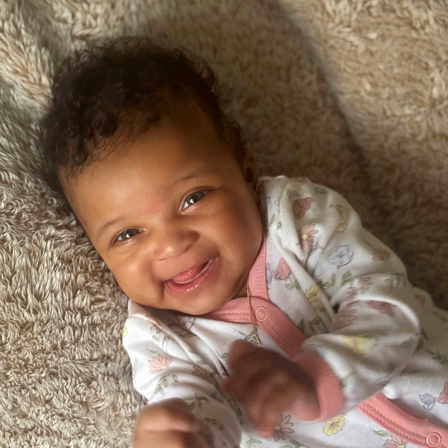 Miyonna is registered to the contest to win money with this photo: baby, blanket, child, closeup, cozy, curly_hair, cute, face, floral_pattern, hands, happy, indoors, infant, lying_down, onesie, playful, portrait, skin, smiling, soft_texture