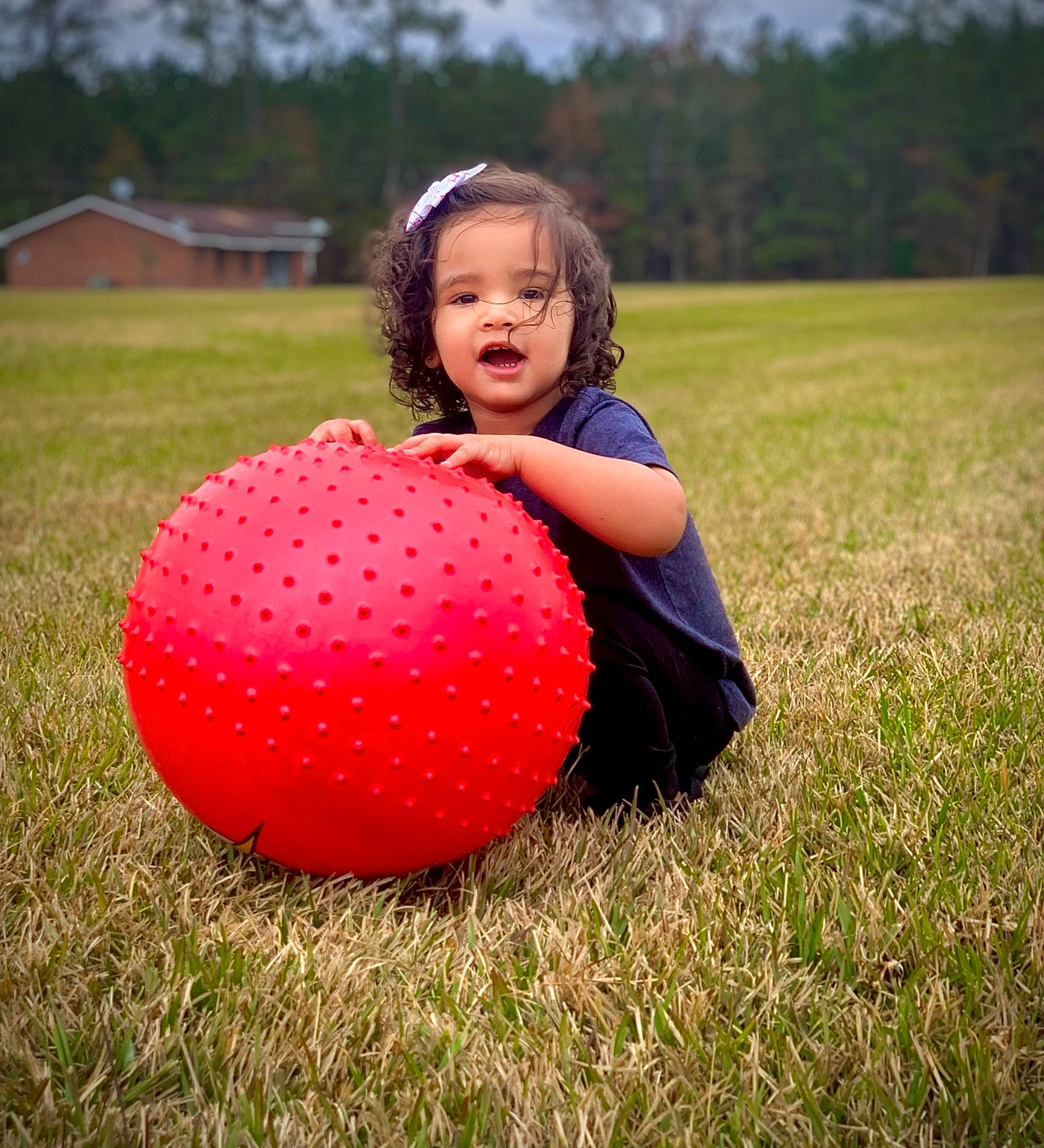 Annalyn is registered to the contest to win money with this photo: baby_toddler_clothing, ball, blond, flash_photography, fun, grass, grassland, happy, lawn, leisure, meadow, people_in_nature, person, plant, prairie, recreation, sitting, sky, sports_equipment, toddler