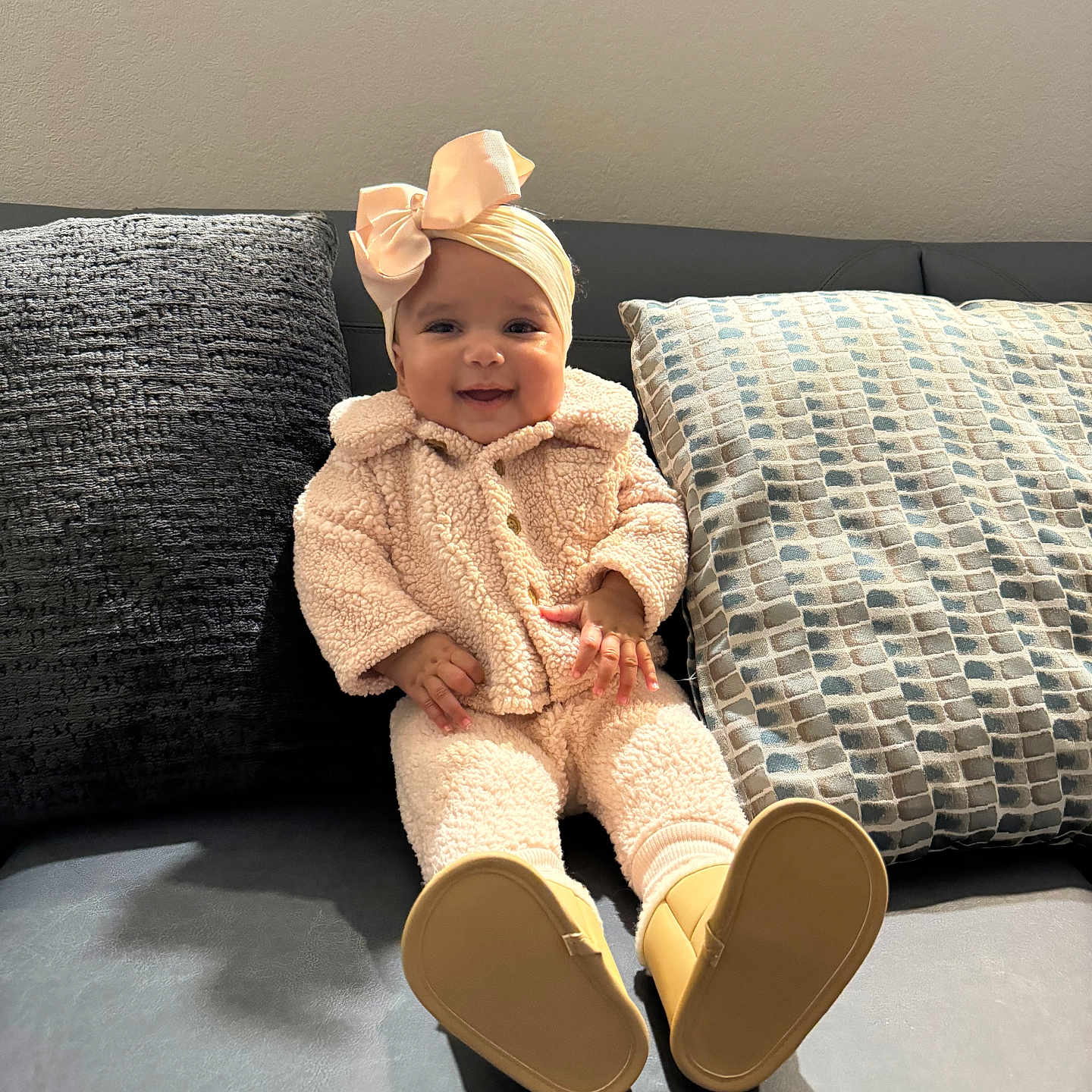 Ava is registered to the contest to win money with this photo: baby, bonnet, cap, clothing, couch, face, footwear, furniture, happy, hat, head, knitwear, pants, person, photography, portrait, shoe, sitting, smile, sweater