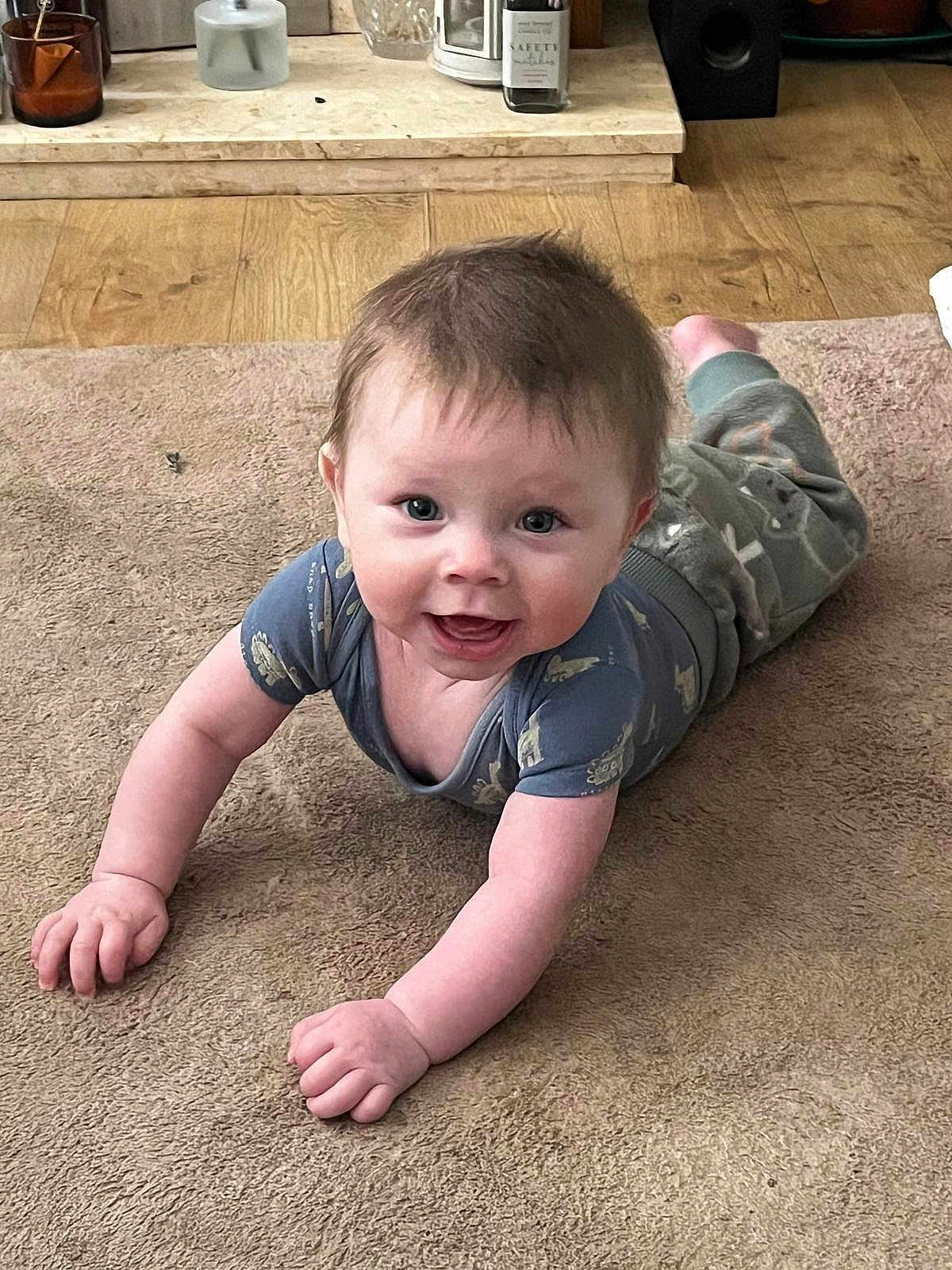 Lucas is registered to the contest to win money with this photo: baby, infant, carpet, floor, smiling, happy, indoors, child, person, clothing, wood_floor, home, crawling, cute, young, face, eyes, arms, pants, tshirt