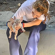 Ace is registered to the contest to win money with this photo: person, puppy, dog, outdoor, tree, rock, concrete, casual_clothing, sneakers, smiling, pet, nature, young_adult, holding, sunlight, daytime, crouching, cute, animal, happy