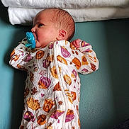 Estella is registered to the contest to win money with this photo: baby, infant, pacifier, onesie, autumn, pumpkin, sunflower, towel, hand, teal_surface, sleepwear, newborn, cute, child, patterned_clothing, lying_down, small_hands, soft_texture, cozy, portrait
