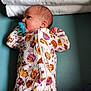 baby, infant, pacifier, onesie, autumn, pumpkin, sunflower, towel, hand, teal_surface, sleepwear, newborn, cute, child, patterned_clothing, lying_down, small_hands, soft_texture, cozy, portrait