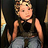 child, toddler, baby, car_seat, sitting, portrait, face, eyes, looking_up, curious, cow_print, hat, shoes, jeans, cargo_pants, seatbelt, indoors, vehicle, fashion, smiling