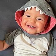 Donovan joined the competition — help win amazing prizes! baby, child, smiling, hoodie, shark_hood, teeth, couch, gray, clothing, infant, cute, happy, portrait, sitting, indoors, face, apparel, young_child, playful, casual