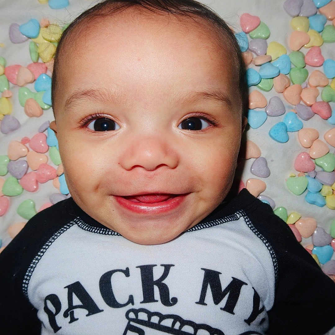 Abdul-Malik is registered to the contest to win money with this photo: baby, background, big_eyes, candy_hearts, cheeks, closeup, clothing, cute, dimples, face, happy, heart_shapes, infant, lying_down, onesie, pastel, playful, portrait, skin, smiling