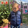 toddler, child, blue_vest, jeans, sneakers, gravel, garden, flowers, plants, butterfly, pink_door, outdoor, daylight, fence, greenery, casual_clothing, sunlight, portrait, cute, young_child