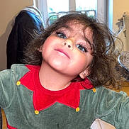 Ilenka a rejoint le concours — aidez-le/la à gagner de superbes lots ! child, face, portrait, indoor, window, clothing, green_dress, red_collar, curly_hair, smile, person, young_child, playful, cute, home, furniture, floor_tiles, jacket, light, casual