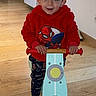 Kingsley participe au concours pour gagner de l'argent avec cette photo : child, toddler, indoor, balance_bike, red_hoodie, spiderman, wooden_floor, smiling, toy, person, window, clothing, play, footwear, hair, furniture, home, flooring, handlebars, cute