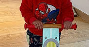 Kingsley a rejoint le concours — aidez-le/la à gagner de superbes lots ! toddler, child, indoors, balance_bike, red_hoodie, spiderman, wooden_floor, smiling, toy, playful, window, towel, pants, green_socks, person, young_child, flooring, handlebars, home, casual