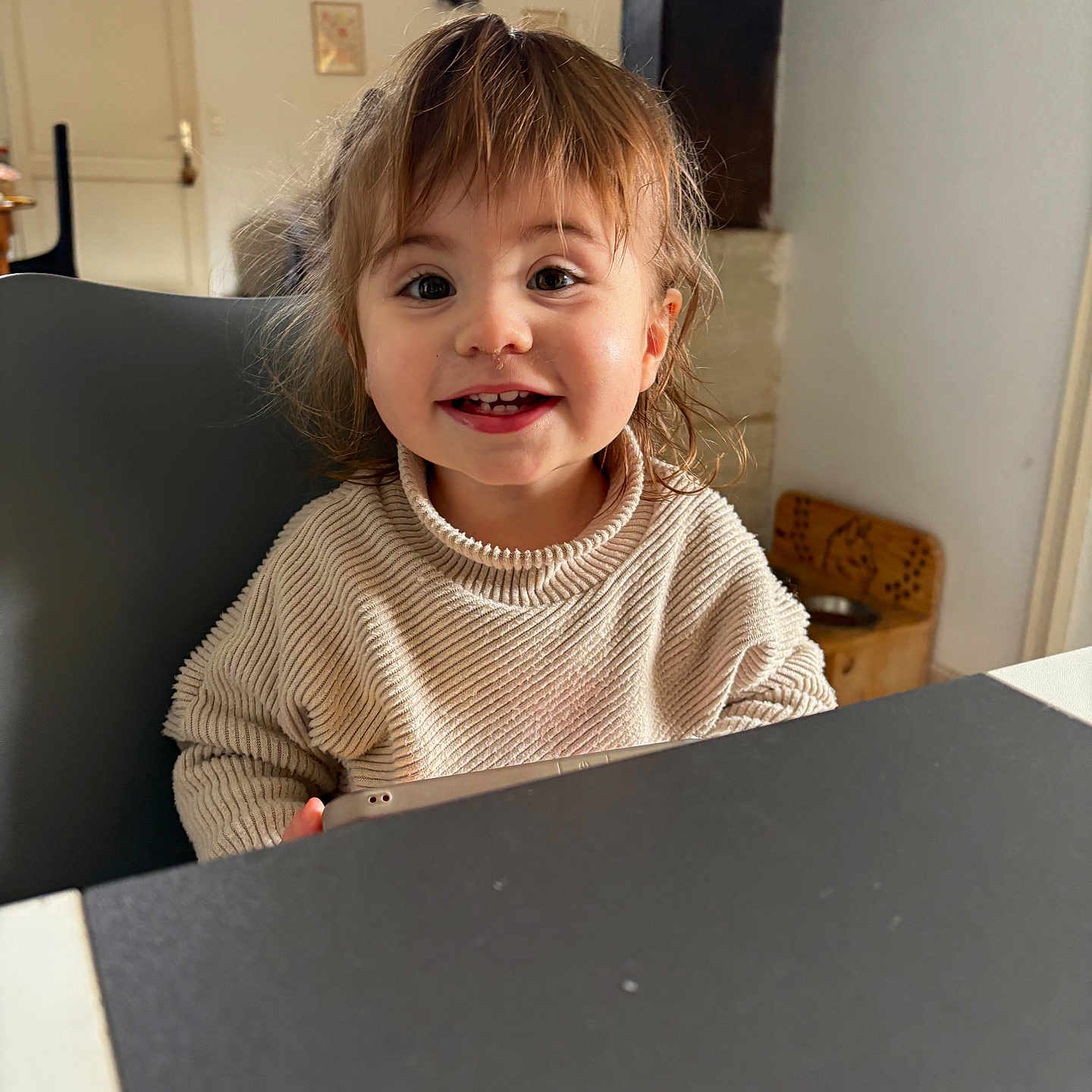 Meilya participe au concours pour gagner de l'argent avec cette photo : bangs, brown_hair, chair, child, cute, door, face, furniture, happy, indoor, portrait, smile, smiling, sweater, table, tablet, tabletop, teeth, toddler, window