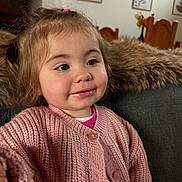 Meilya a rejoint le concours — aidez-le/la à gagner de superbes lots ! toddler, child, pink_sweater, knitted_clothing, smiling, face, portrait, couch, blanket, indoor, home_decor, wooden_chair, furniture, curly_hair, happy, baby, cozy, casual_clothing, person, seated