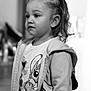 child, toddler, portrait, black_and_white, braided_hair, pony_tail, jacket, cartoon_tshirt, indoor, person, face, expression, young_child, cute, clothing, standing, looking_away, soft_focus, monochrome, casual