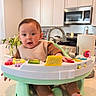 baby, child, infant, kitchen, activity_walker, toy, sitting, face, portrait, wide_eyes, open_mouth, brown_hair, bib, clothing, bare_feet, furniture, cabinets, sink, microwave, houseplant