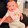 baby, child, infant, adult, sitting, lap, portrait, blue_bows, pink_bib, smiling, wide_eyes, indoor, home, chair, clothing, pants, socks, family, human, photography