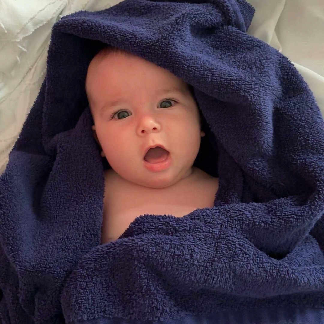João participe au concours pour gagner de l'argent avec cette photo : baby, bedspread, blue_towel, child, cozy, cute, expression, face, head, indoor, infant, person, portrait, skin, soft, surprised, texture, towel, white, wrapped