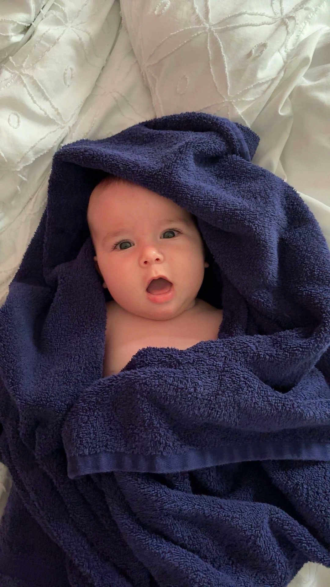 João participe au concours pour gagner de l'argent avec cette photo : baby, towel, blue_towel, wrapped, surprised, expression, face, head, skin, infant, bedspread, white, texture, soft, cozy, indoor, person, child, portrait, cute