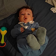 Sipan participe au concours pour gagner de l'argent avec cette photo : baby, infant, blue_outfit, bow_tie, lying_down, bed, blanket, toy, rattle, sock, cute, child, indoor, expression, person, fabric, head, face, hand, feet