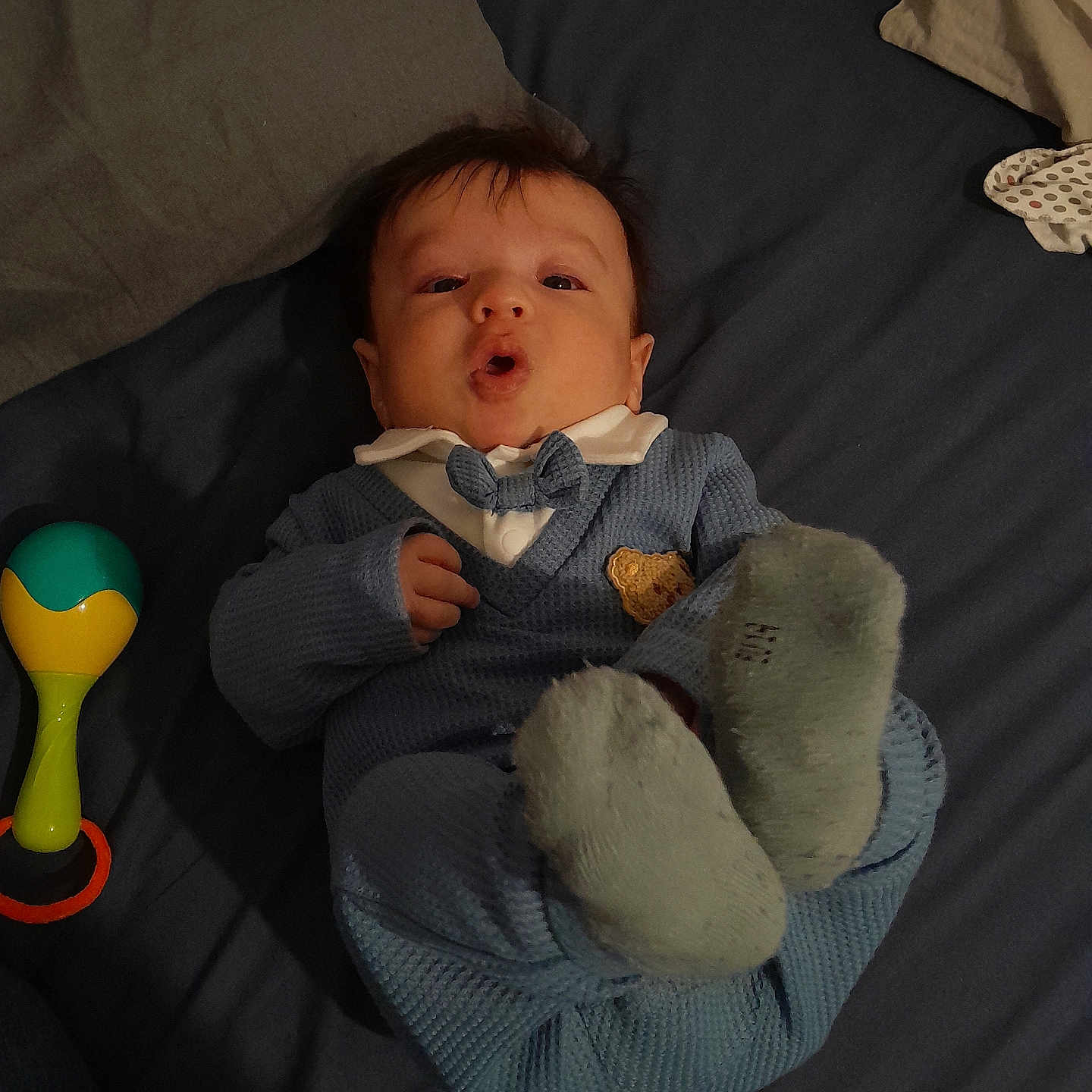 Sipan participe au concours pour gagner de l'argent avec cette photo : baby, bed, blanket, blue_outfit, bow_tie, child, cute, expression, fabric, face, feet, hand, head, indoor, infant, lying_down, person, rattle, sock, toy