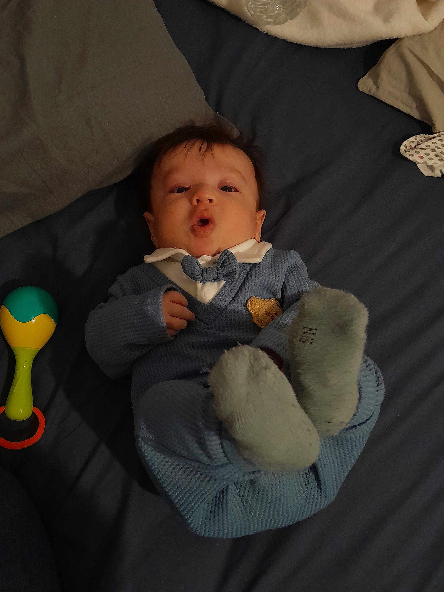Sipan participe au concours pour gagner de l'argent avec cette photo : baby, infant, blue_outfit, bow_tie, lying_down, bed, blanket, toy, rattle, sock, cute, child, indoor, expression, person, fabric, head, face, hand, feet