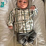 baby, infant, plaid_shirt, gray_pants, white_socks, towel, pacifier_clip, lying_down, indoors, curious_expression, child, young, cute, soft_texture, casual_clothing, small_hands, wide_eyes, head, face, resting