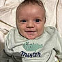 baby, smiling, face, infant, sweater, clothing, crocodile_print, text_on_clothing, soft_blanket, cozy, cute, portrait, indoor, happy, child, young, human, person, head, expression
