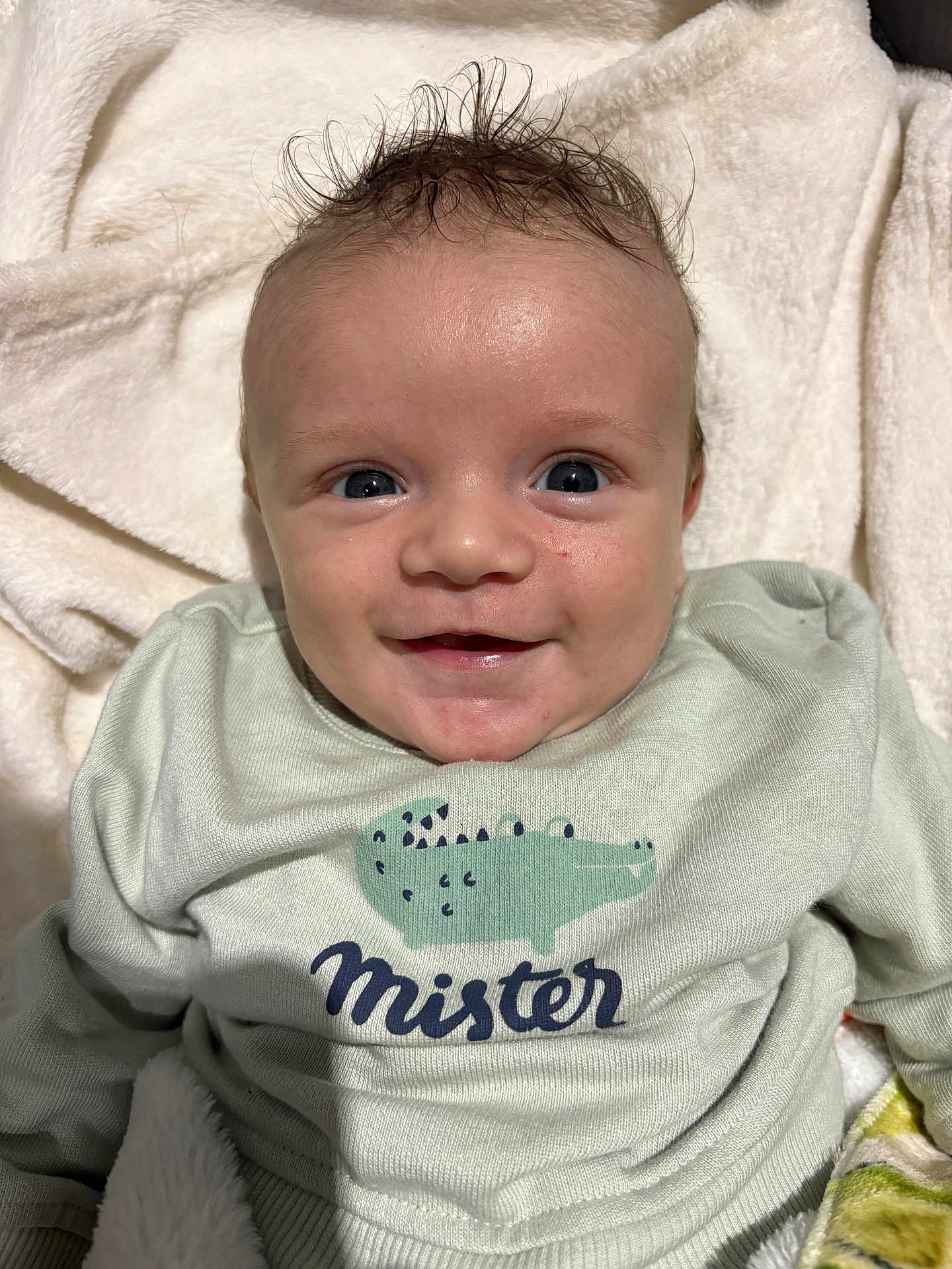 Eliot participe au concours pour gagner de l'argent avec cette photo : baby, smiling, face, infant, sweater, clothing, crocodile_print, text_on_clothing, soft_blanket, cozy, cute, portrait, indoor, happy, child, young, human, person, head, expression