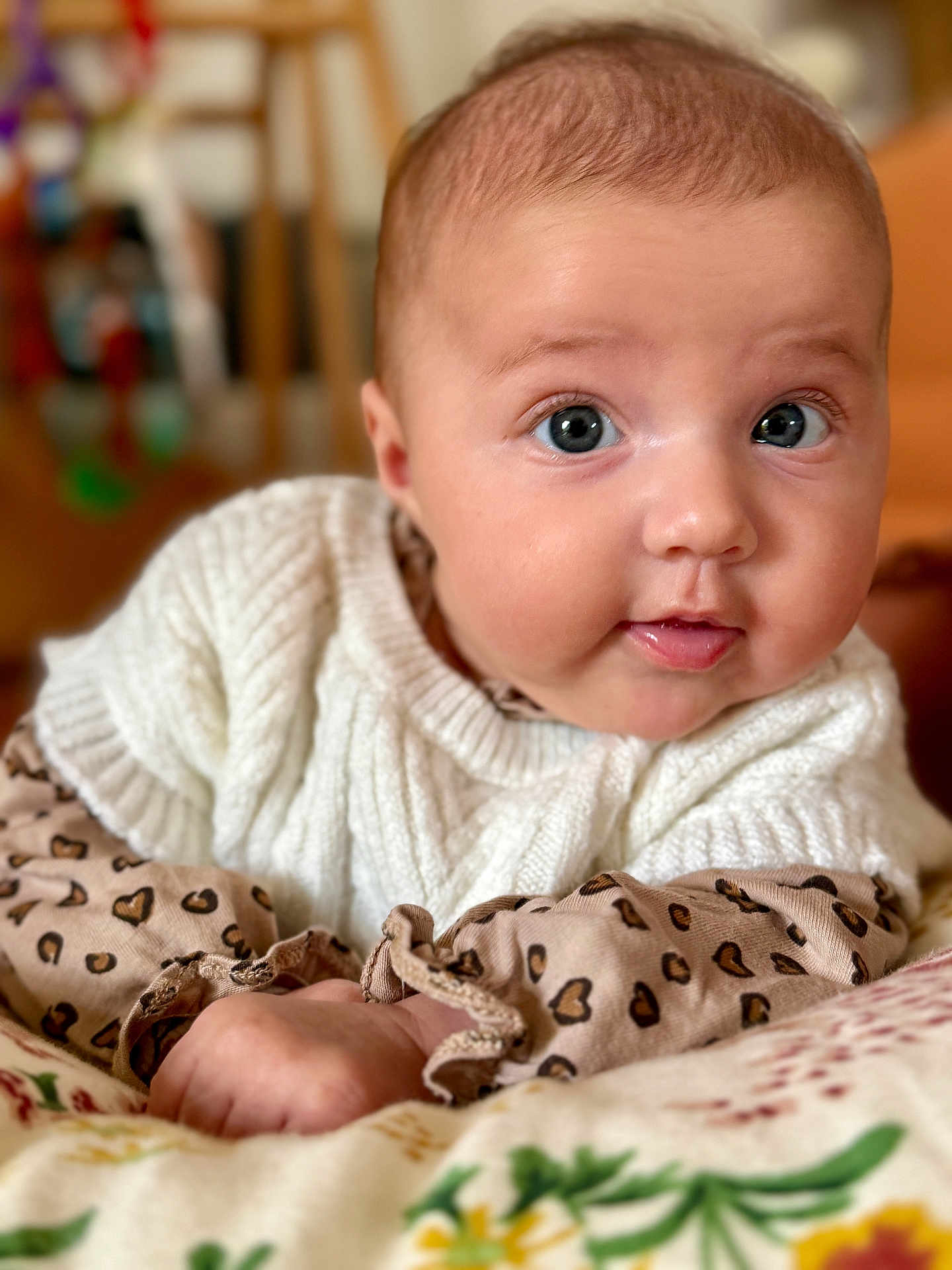 Agathe participe au concours pour gagner de l'argent avec cette photo : baby, infant, face, eyes, sweater, knitted, patterned_clothing, heart_pattern, blanket, floral, cute, chubby_cheeks, lying_down, indoor, portrait, close_up, child, person, skin, soft_light