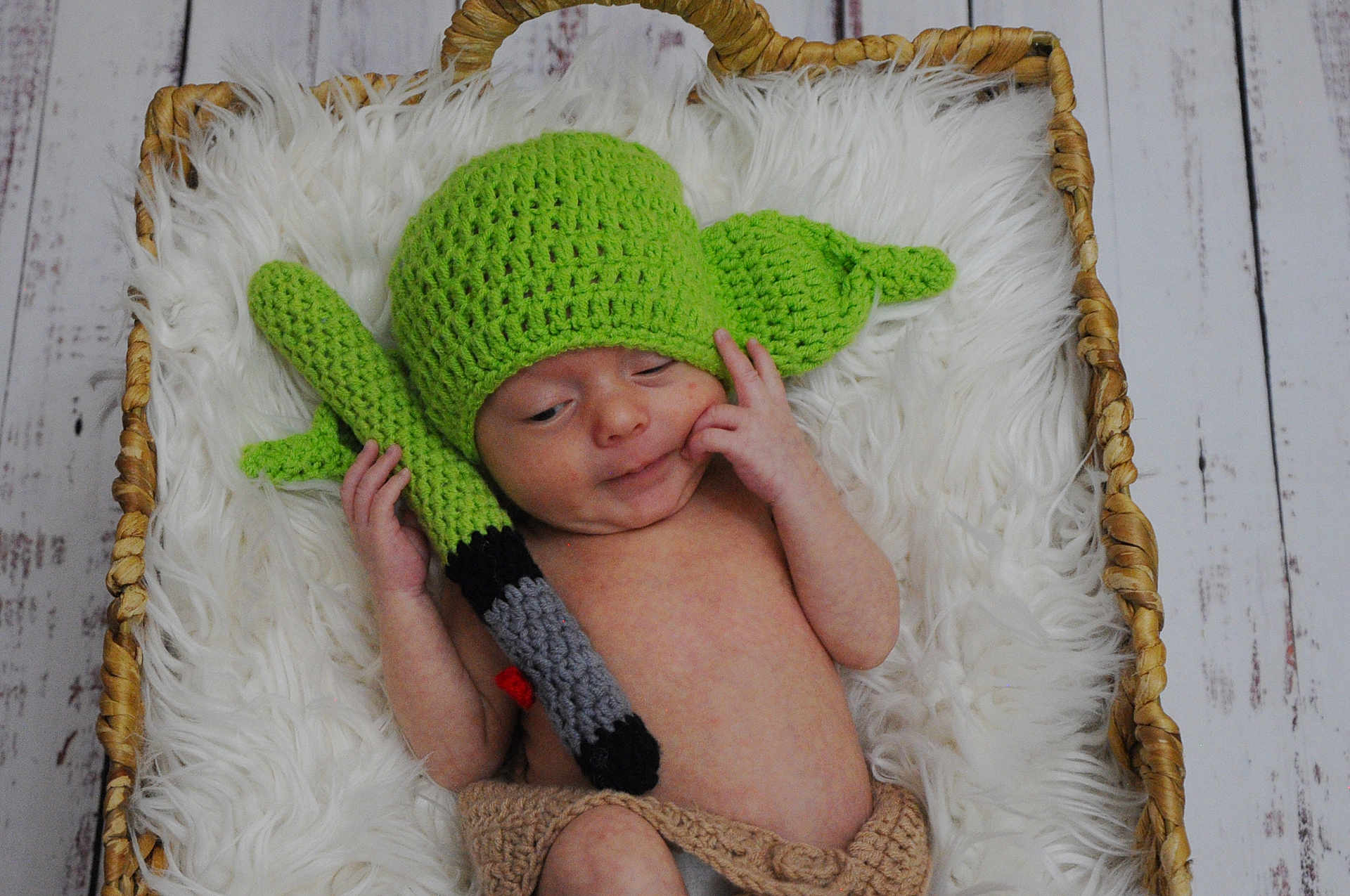 Oakley is registered to the contest to win money with this photo: baby, infant, basket, crochet, hat, light_saber, costume, green, hand, face, skin, fur, wooden_floor, blanket, cute, lying_down, newborn, indoors, soft, props
