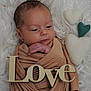 baby, newborn, wrapped, brown_cloth, wooden_sign, love, felt_hearts, white_fur, soft_texture, peaceful, infant, portrait, cute, resting, indoor, cozy, child, human, small, adorable